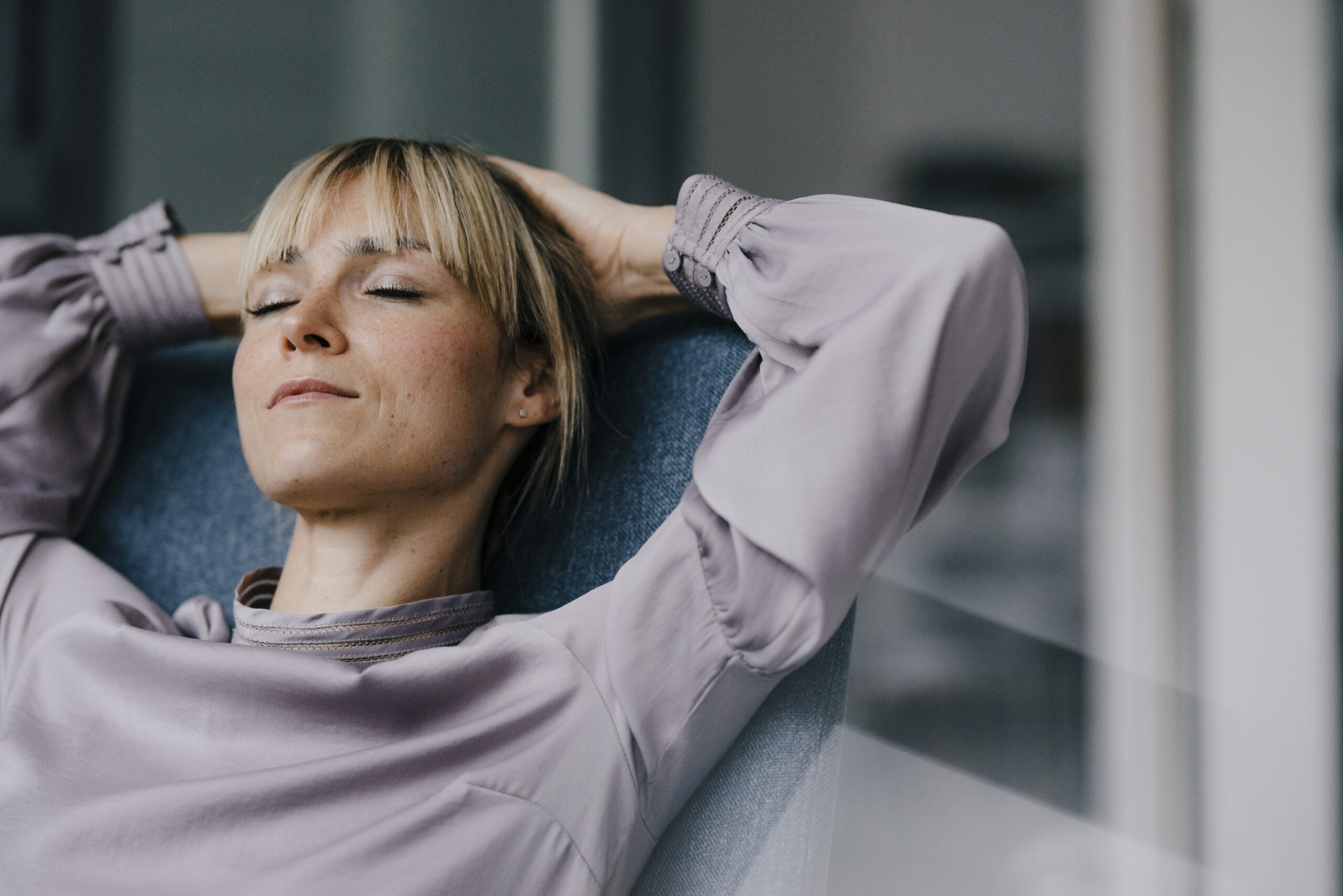 Blond woman relaxing in armchair with hands behind head Acceptance Path Counseling A woman leans back in a chair with her eyes closed and hands behind her head appearing calm and at peace