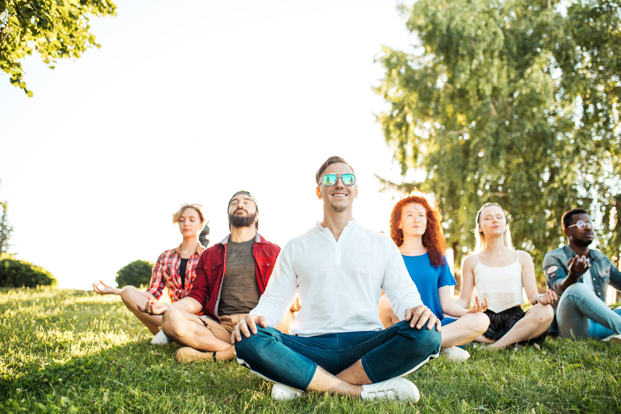 A diverse group of people practicing outdoor meditation in a park demonstrating the communal and mental health benefits of mindfulness for residents in the Houston Willowbrook area