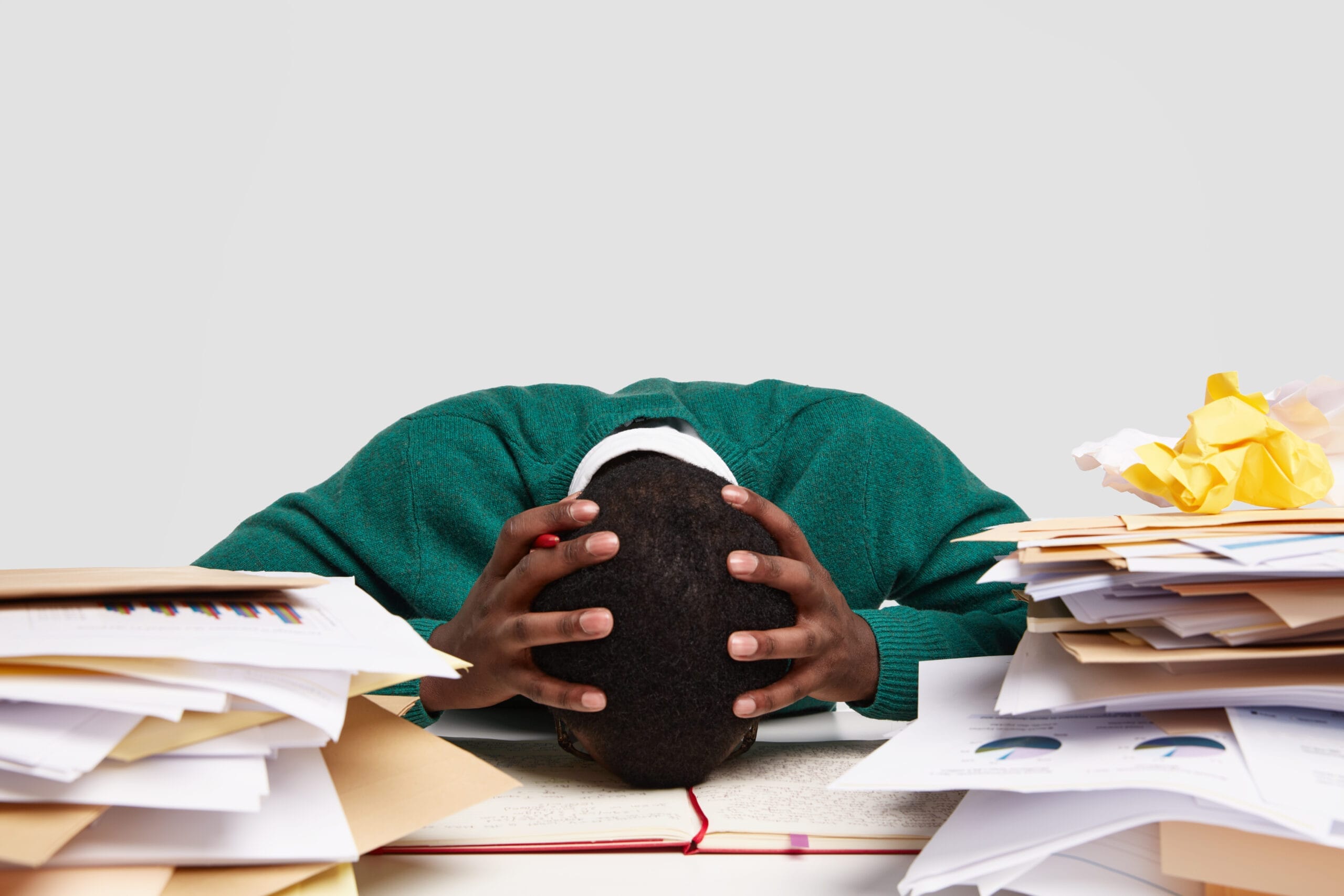 A person with their head on a desk overwhelmed by stacks of paperwork symbolizing the stress that Houston Willowbrook professionals can manage through the benefits of mindfulness