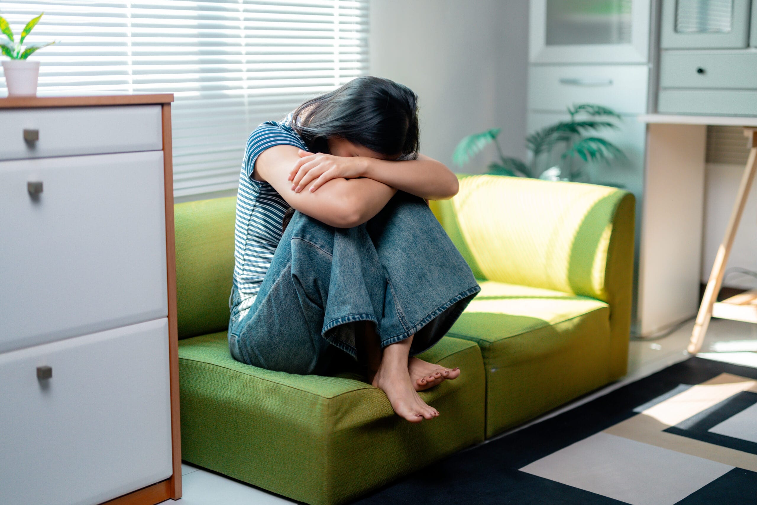 A woman huddles in distress on a green sofa beneath the headline Can OCD Cause Depression