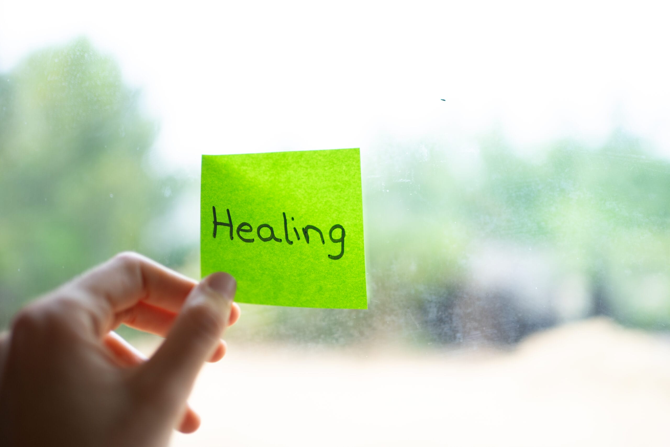 Woman applying healing note on window glass during daytime Acceptance Path Counseling Acceptance Path Counseling A sticky note labeled Healing representing the first step in learning how to heal from trauma for professionals in Sterling Ridge