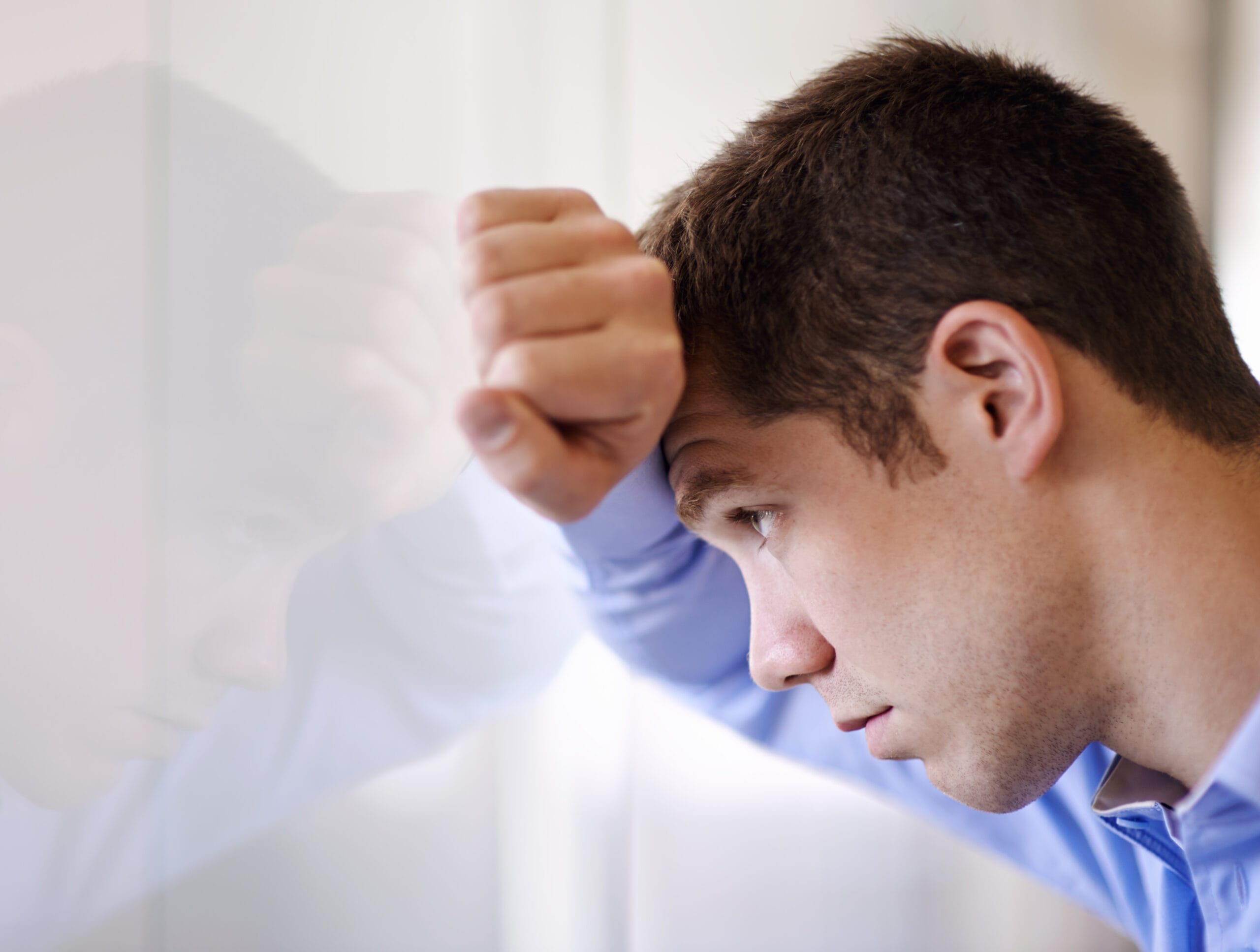 A man leaning his forehead against a mirrored or reflective wall illustrating the internal conflict and struggle against intrusive thoughts and mental loops